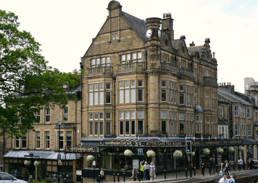  Betty's Cafe Tea Rooms by Neil Turner. An imposing three-storey stone building forms the block corner, with intricately carved bay windows and Betty's Cafe and Tea Rooms below. The cafe has full-length windows with black gloss frames, its name etched out in gold.