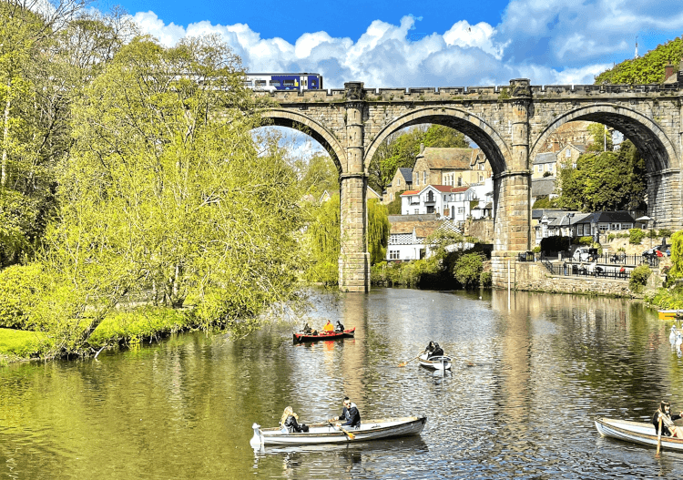 People boat on the river beneath the Knaresborough Viaduct on a sunny day.