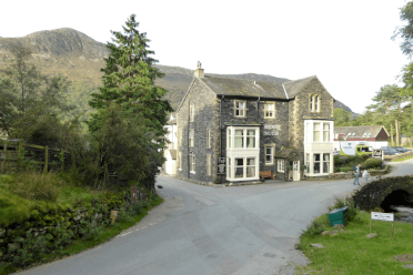 Bridge Hotel, Buttermere, by Andrew Bowden. At the end of a drive, framed by the fells, stands a large white-timbered hotel built from grey stone.