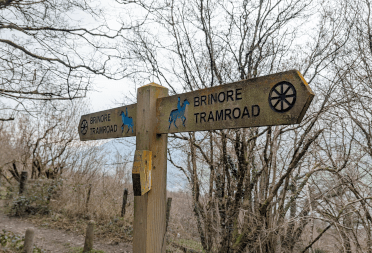 The wooden Brinore Tramway fingerpost, carved with the bridleway horse and rider symbol and a spoked wheel.
