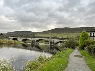 An arched stone bridge carries the main road over the River Wharfe at the edge of Burnsall. The Yorkshire hills stand impressively in the background.