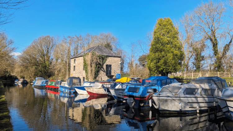 A row of moored narrowboats, brightly painted in a range of colours, at the Govilon Marina on a clear blue day.