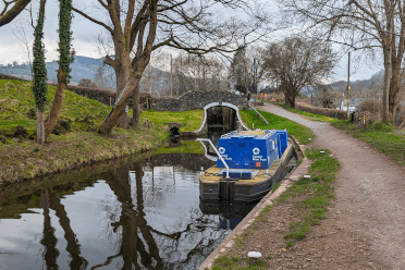 One of the Canal Trust's boast moored on the Brecon and Monmouthshire Canal, with a lock in the background and trees to either side.