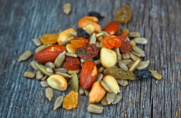 A handful of trail mix, comprised of mixed nuts and seeds, fruit peel and dried fruit, sits on a wooden surface.