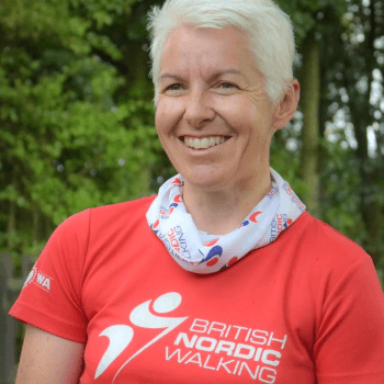 Dr Catherine Hughes of British Nordic Walking stands outside wearing a Nordic Walking branded t-shirt.