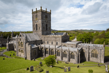 A wide view of St Davids Cathedral, an immaculate old building with multiple wings. It's built in dark stone, paler in the arching stone windowframes, and has a large square tower at its centre. The cathedral sits at the start of the Celtic Way, and can also be visited on our St Davids Short Break walking holiday.