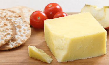 A block of cheese beside some crackers and baby tomatoes.