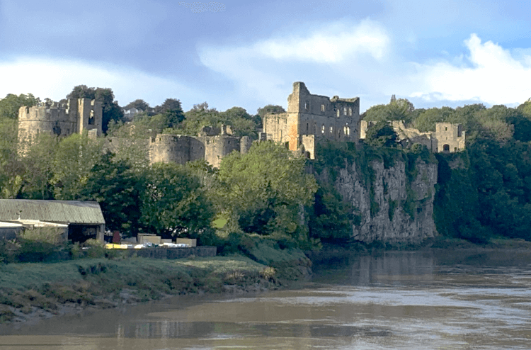 The remarkably complete ruins of Chepstow Castle rise above the River Wye on a bright day.