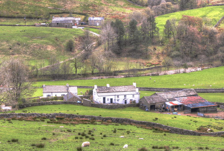 The Sportsman's Inn as viewed from behind: a whitewashed building beside a whitewashed farmhouse and tin barn, surrounded on all sides by the green fields of Yorkshire, patchworked by stone walls.