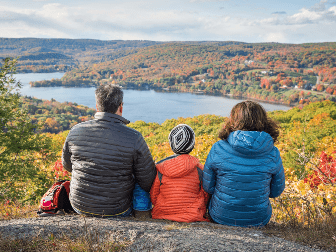 A family sits to admire a forest below.