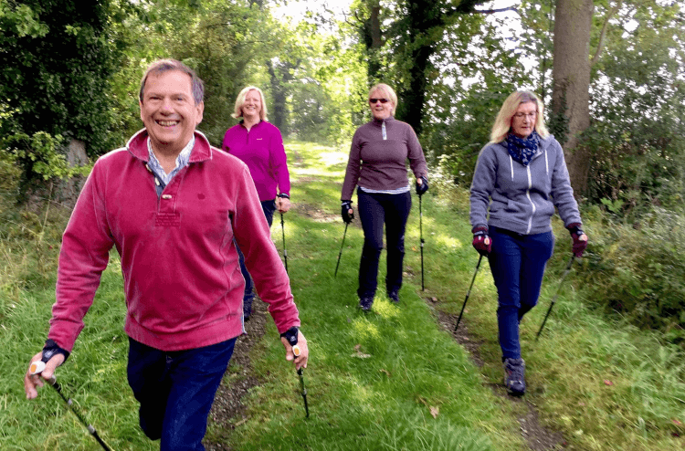 A group of Nordic Walkers beam at the camera as they hike through nature in Britain.