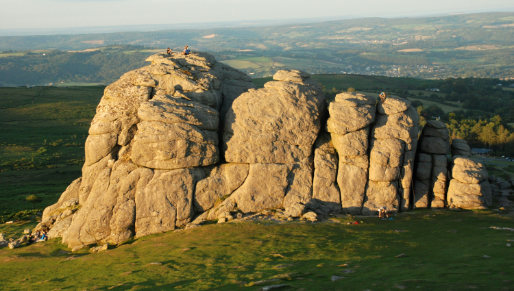 The low sunlight of a winter evening clips across the huge stone protrusion of Haytor in Dartmoor. People look tiny beside this enormous natural structure.