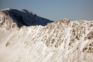 Winter snow transforms Helvellyn and Striding Edge. The sharp rock face is covered in white.