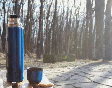 A blue insulated drinks flask sits on a picnic table on a trail.