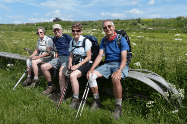 A group of walkers rest on a bench on the Yorkshire Wolds Way in summer walking gear.