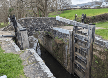 One of the flight of Llangynidr Locks. A photo taken up-close of the wooden gates that close the canal and allow the level to rise. Stone bridge 132 crosses the canal just behind the gate.