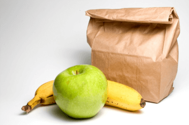 A packed lunch in a paper bag, with an apple and banana sitting beside it.