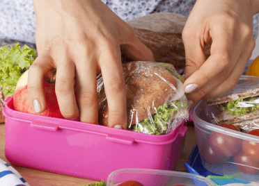 A walker packs a rigid lunchbox with sandwiches for their summer walk.