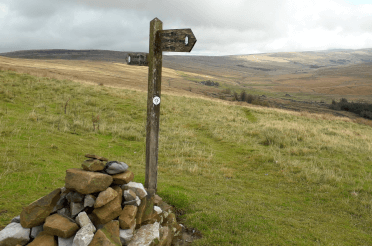 A fingerpost sprouts from a tall cairn built around its base. It signposts an intersection of the Dales Way and the Pennine Way.