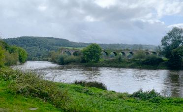 An arched bridge stands in the distance, with the River Wye running calmly in the foreground.