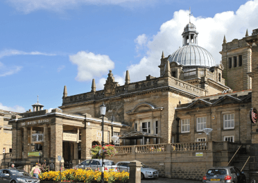 Royal Baths by Tony Hisgett. The Royal Baths in Harrogate as viewed outside, looking across at the grand stone entryway with the domed roof behind.