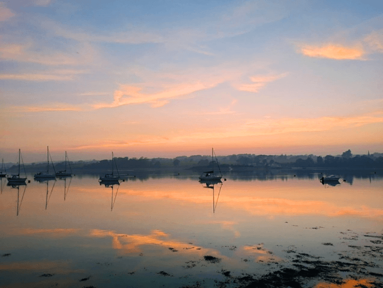 The sky and sea are orange at sunset, with boats bobbing in Y Felinheli harbour.