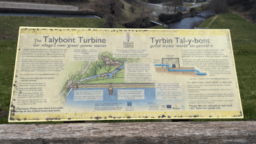 An information board about the Talybont Turbine, with text explaining the purchase of the turbine house and art of the way water runs down from the reservoir to power the turbine.