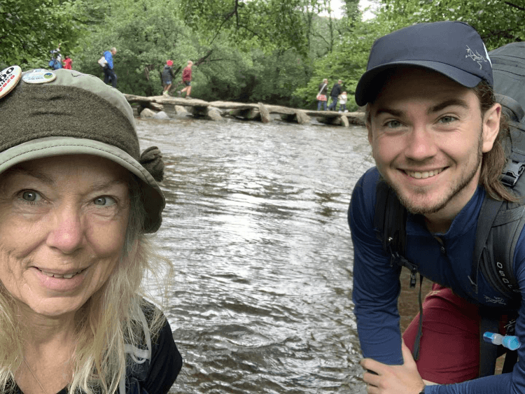 Walkers take a selfie with the Tarr Steps, a bridge made entirely of large slab stone, in the background.