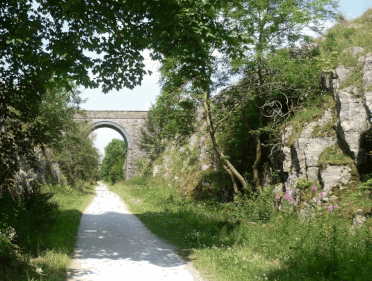 The Tissington Trail, a level, well-surfaced path leading between limestone cliffs and under an old railway viaduct.