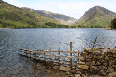 A wooden fence trails down into the water of Buttermere, with lakeland fells standing on the far shore.