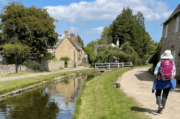 A walker shields herself from the sun with a broad-brimmed hat as she walks through a village on a long-distance walking holiday.