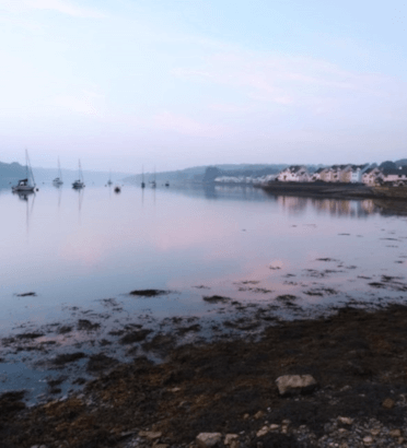 Dusk settles over Y Felinheli harbour, with little houses clustered along the harbour front and boats floating in the glassy water.