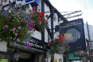 Ye Olde Cheshire Cheese by Adam Bruderer. A close-up of Ye Olde Cheshire Cheese Inn, an old black and white timbered coaching inn wreathed with colourful flowers and signs in ye olde English script. The close-up is of the door and a sign saying muddy boots are welcome.