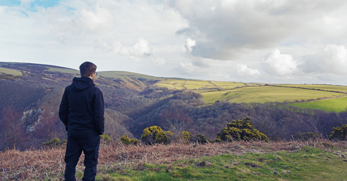 A hiker looks out over a steep-sided wooded valley in Exmoor.